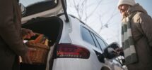 Senior woman charging their electric car, during his husban giving purchase in car trunk.