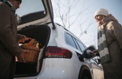 Senior woman charging their electric car, during his husban giving purchase in car trunk.