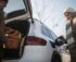 Senior woman charging their electric car, during his husban giving purchase in car trunk.
